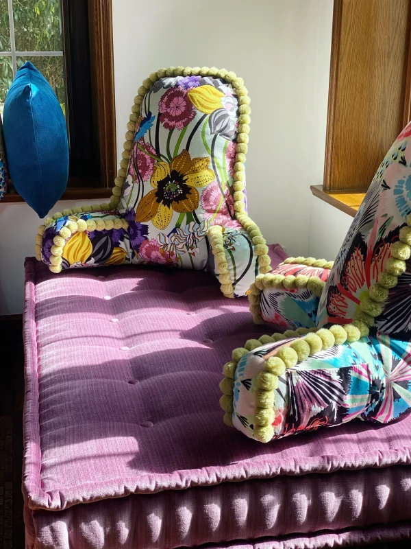 Side profile of a French Mah Jong daybed with purple and blue cushions, styled with a textured green backrest in a vibrant living space