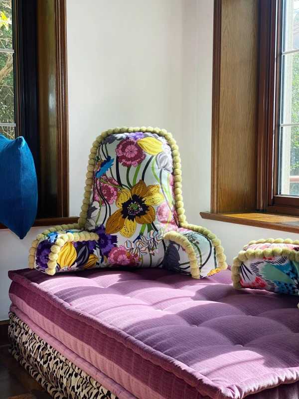 Colorful French daybed Mah Jong sofa with layered cushions and backrests in a cozy living room, featuring vibrant fabrics and a fireplace in the background