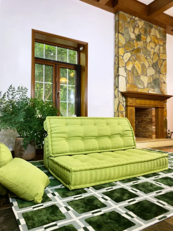 Green Mah Jong daybed in a bright room with a stone fireplace, decorative plants, and soft cushions.