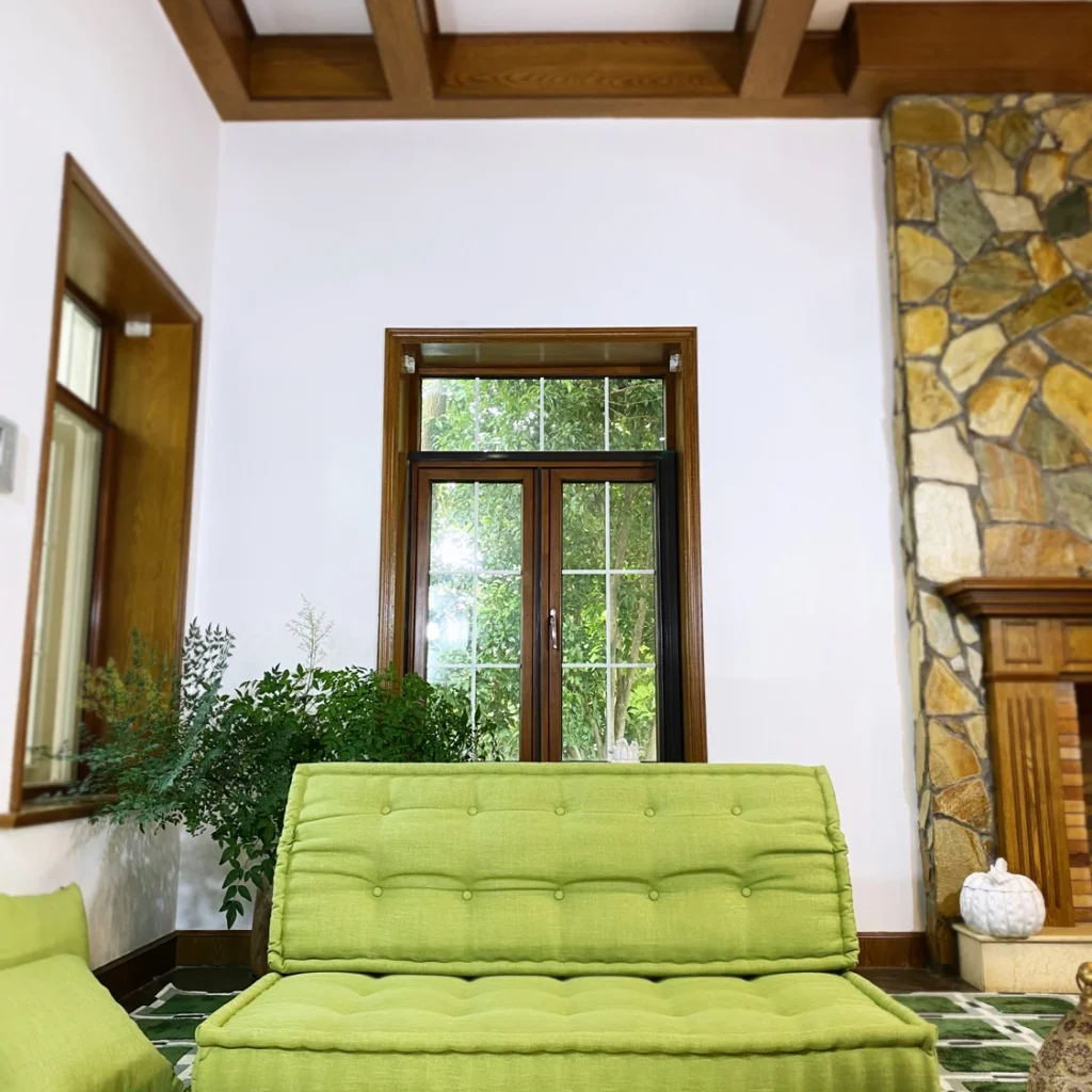 Bright green French Mah Jong daybed with tufted cushions in a living room with wooden beams and natural decor.
