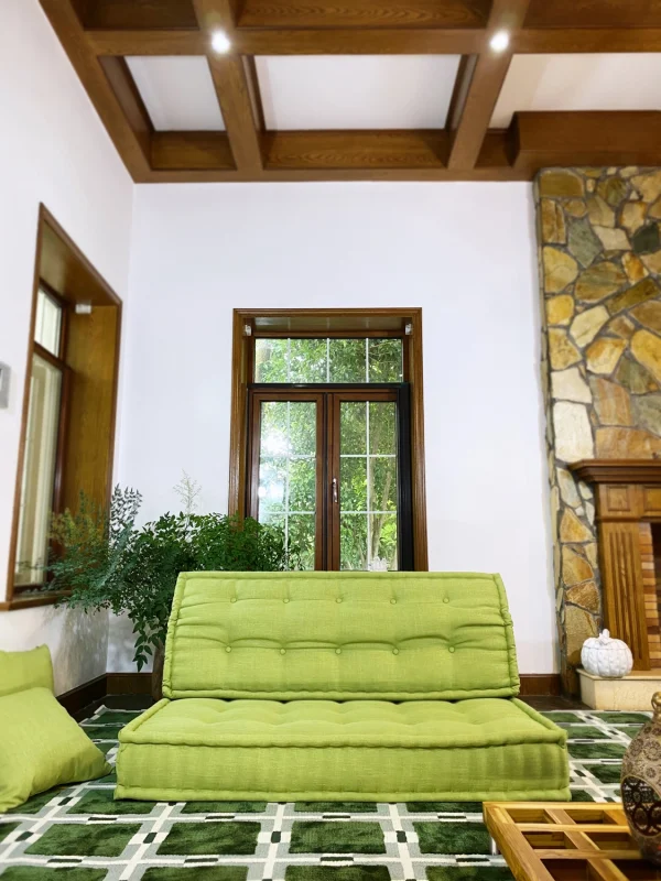 Bright green French Mah Jong daybed with tufted cushions in a living room with wooden beams and natural decor.