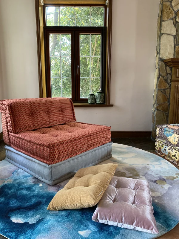 Rust-colored Mah Jong sofa styled on a watercolor-inspired rug with pastel throw cushions in a sunlit living room