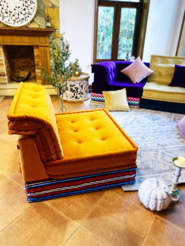 Bright yellow Mah Jong daybed with layered striped cushions, styled in a cozy living room with a fireplace and vibrant decor.