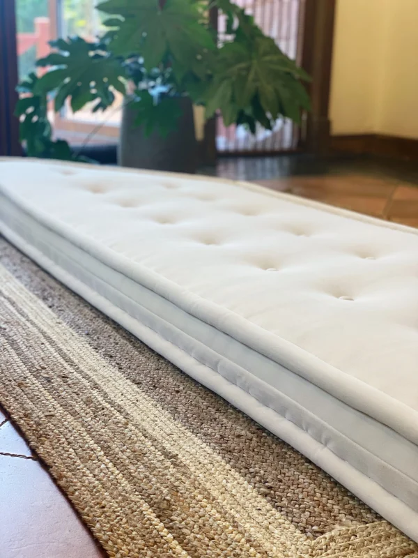 Stacked white cushions of the French daybed Mah Jong sofa with colorful cushions in the background.