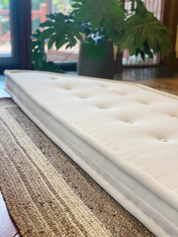 Side profile of the French daybed Mah Jong sofa in white, resting on a woven rug.