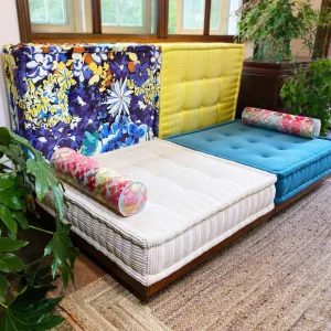 Dual-colored Mah Jong Sofa with colorful floral bolsters, bold backrests, and natural rug flooring.