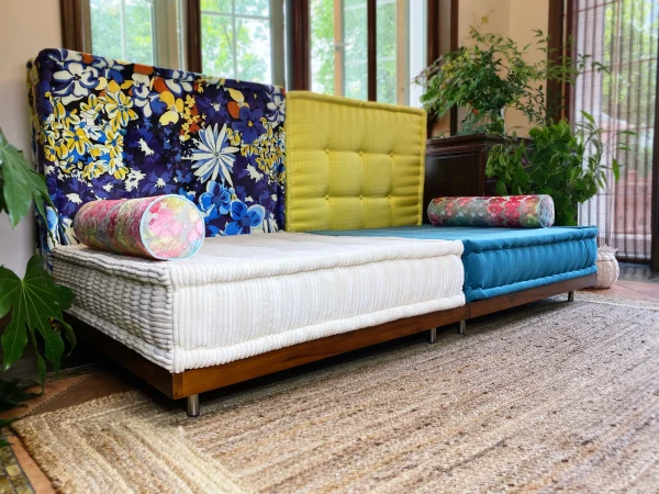 Close-up view of the Mah Jong Sofa with white and blue cushions and floral bolsters on a natural rug.