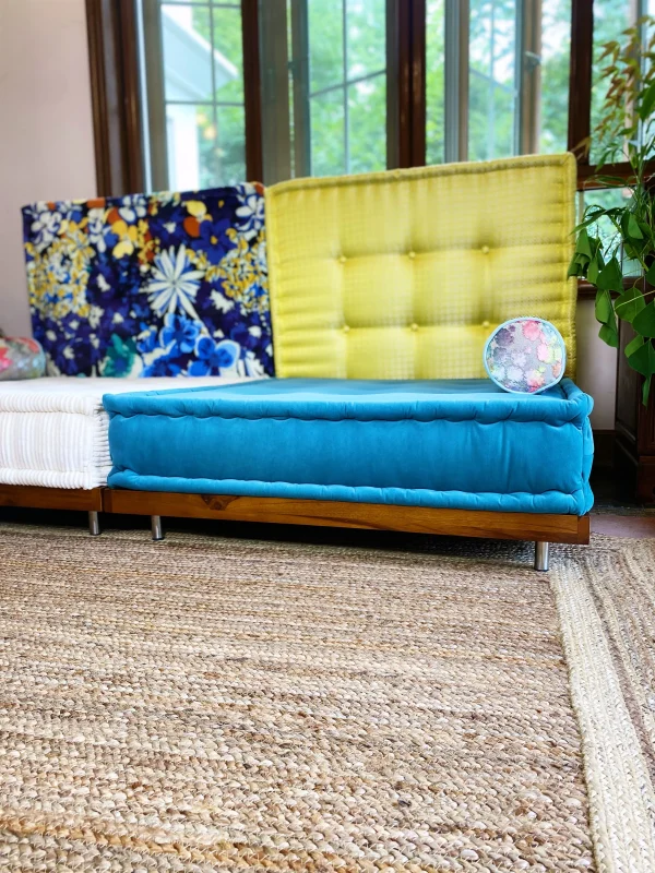 Modern Mah Jong Daybed Sofa styled with blue and white cushions, yellow and floral backrests, and green plants.