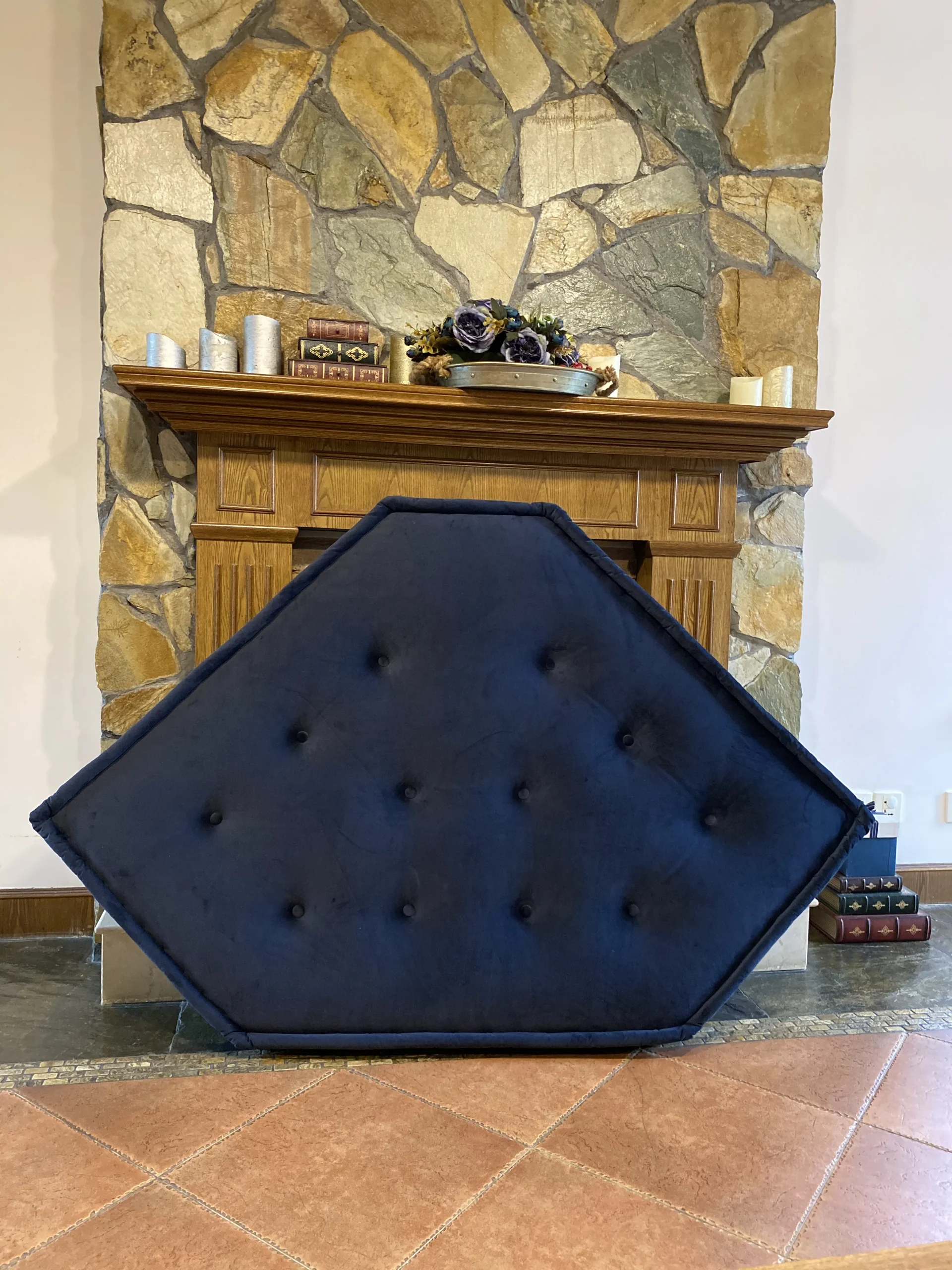 A navy blue tufted corner mat from the French Daybed Mah Jong sofa collection displayed in front of a rustic stone fireplace.