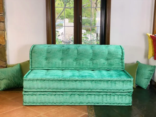 Side angle of a turquoise French Mah Jong daybed with a backdrop of natural light and a modern living space.