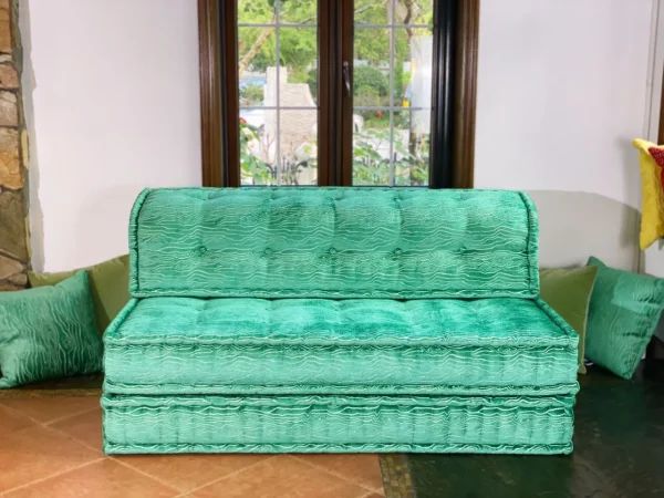 Plush turquoise Mah Jong daybed with elegant tufted details, paired with green cushions in a bright room.