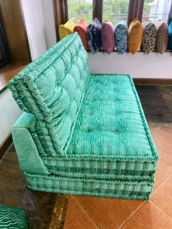 French turquoise daybed with tufted cushions and vibrant upholstery, styled by a window with outdoor views.