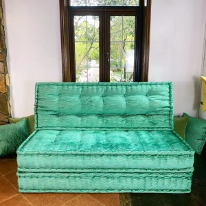 Turquoise French Mah Jong daybed with textured upholstery and tufted cushions, placed in a cozy room with large windows.