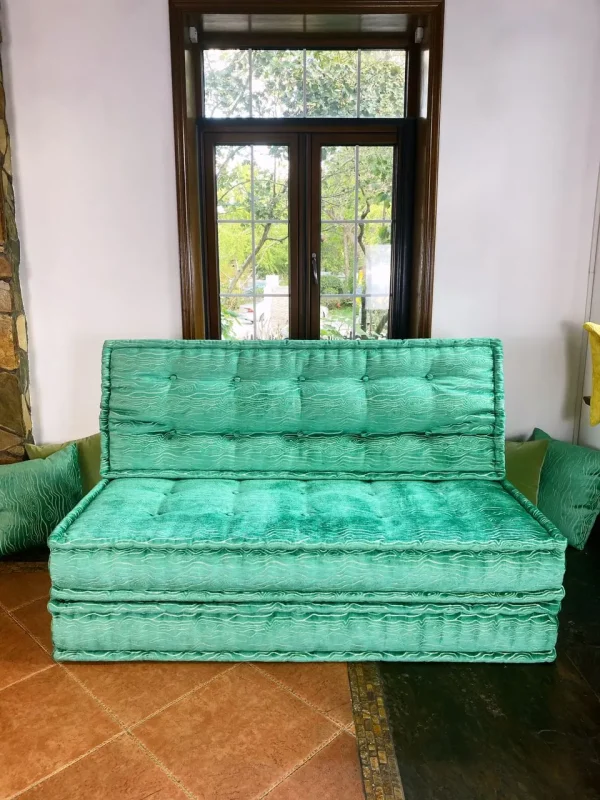 Turquoise French Mah Jong daybed with textured upholstery and tufted cushions, placed in a cozy room with large windows.