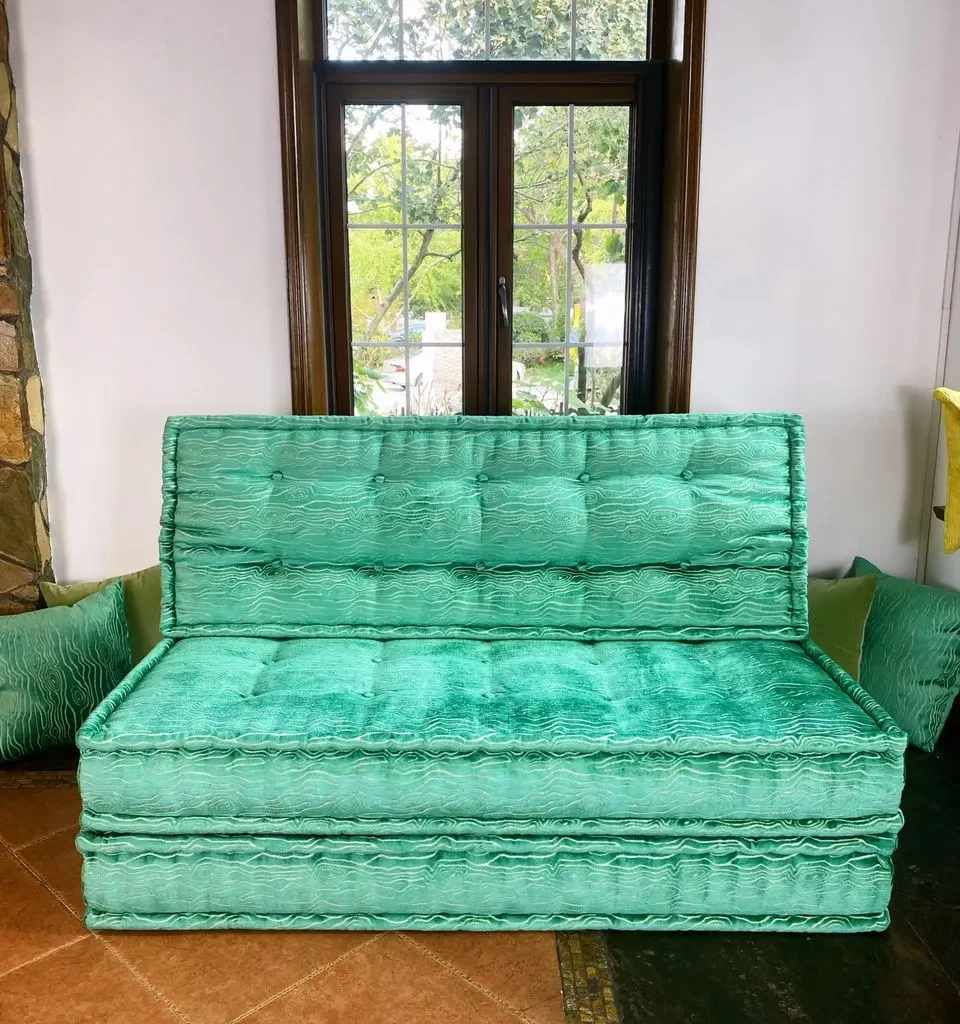 Turquoise French Mah Jong daybed with textured upholstery and tufted cushions, placed in a cozy room with large windows.