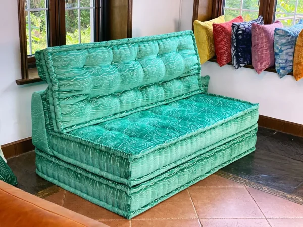 Vibrant turquoise Mah Jong daybed with plush cushioning, complemented by colorful throw pillows in a bright corner space.