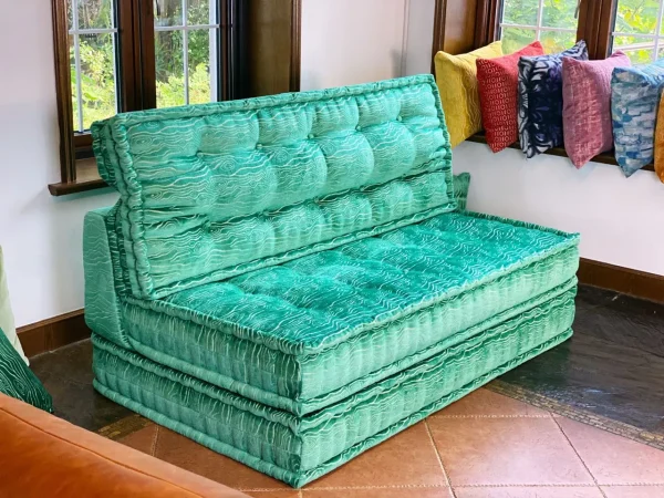 Close-up of a turquoise Mah Jong daybed with intricate fabric patterns and soft padding, highlighted by natural light.