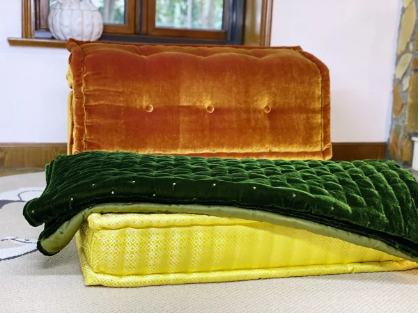 Folded green velvet throw with soft lining placed on a vibrant yellow Mah Jong sofa cushion.