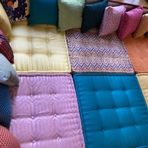 A full view of a vibrant Mah Jong daybed with layered, tufted cushions in orange, turquoise, and yellow tones.