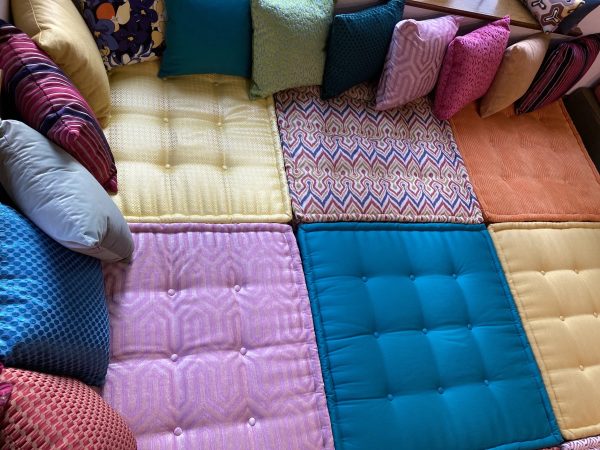 A full view of a vibrant Mah Jong daybed with layered, tufted cushions in orange, turquoise, and yellow tones.