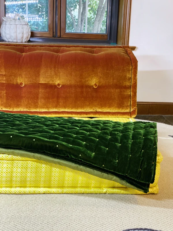 Mah Jong sofa with green velvet throw draped over orange and yellow cushions, styled near a bright window.