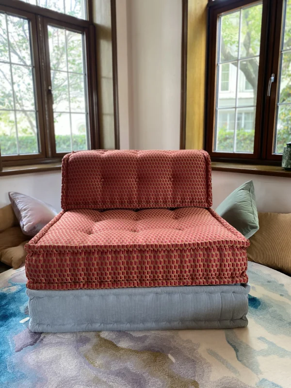 Vibrant yellow and orange Mah Jong daybed styled in an outdoor garden setup, surrounded by lush greenery and soft cushions.