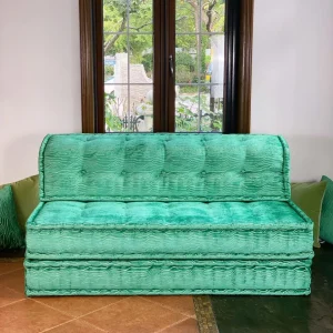 French turquoise Mah Jong daybed with a sleek and minimalist design, placed in front of a window with garden views.