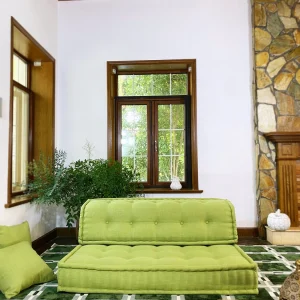 French Mah Jong daybed in vibrant green, placed on a patterned green carpet, surrounded by natural light and decorative elements.