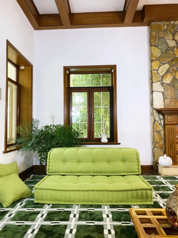 French Mah Jong daybed in vibrant green, placed on a patterned green carpet, surrounded by natural light and decorative elements.