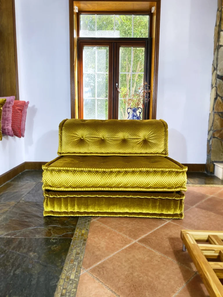 French Mah Jong daybed with golden-yellow upholstery, complemented by a classic blue vase and warm ambient lighting.