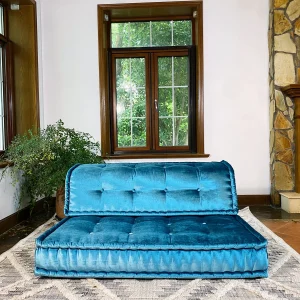 French daybed Mah Jong sofa in teal velvet upholstery, styled in a cozy living room with wooden-framed windows and greenery.