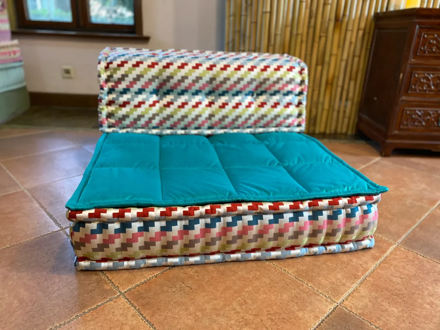 Multicolored patterned Mah Jong sofa with aqua cushion and artistic fabric design.