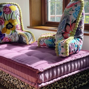 French daybed Mah Jong sofa with vibrant stacked cushions in blue, pink, and yellow patterns, with backrests and a cozy living room setup.