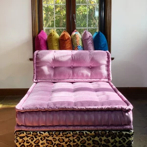 Pink tufted Mah Jong daybed with a leopard print base, framed by a sunny window and colorful pillows.