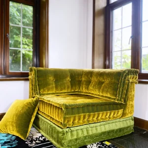 Green velvet Mah Jong daybed with a matching throw pillow on a patterned rug near a window.