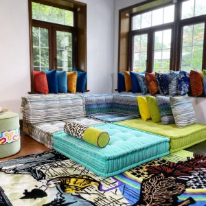 Multicolored Mah Jong sofa with striped upholstery, paired with a leopard print bolster and vibrant cushions, styled on a bold patterned rug.