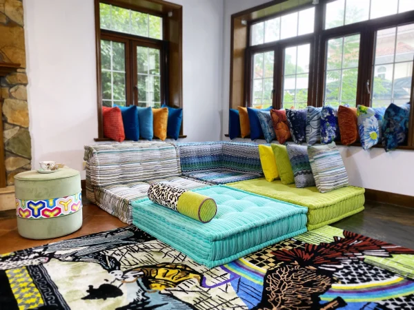 Multicolored Mah Jong sofa with striped upholstery, paired with a leopard print bolster and vibrant cushions, styled on a bold patterned rug.