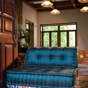 Teal Mah Jong single-mat sofa with a floral patterned base, placed in a rustic entryway with wooden beams and warm ambient lighting.