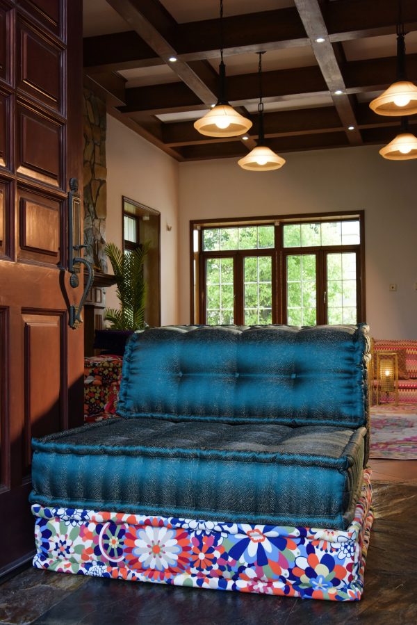 Teal Mah Jong single-mat sofa with a floral patterned base, placed in a rustic entryway with wooden beams and warm ambient lighting.