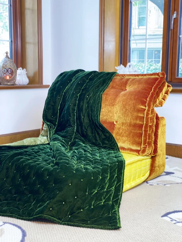 Front view of Mah Jong daybed sofa with green velvet upholstery and plush quilting, styled in a bright living room.