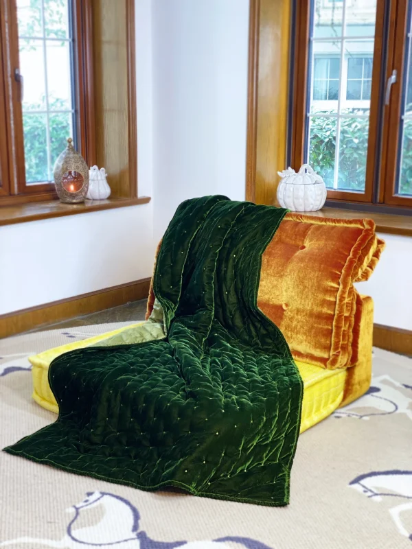 Mah Jong sofa with green velvet throw draped over orange and yellow cushions, styled near a bright window.