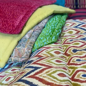Layered fabric swatches of Mah Jong cushions in colorful patterns and textures.