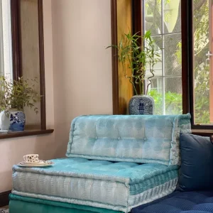 Light blue Mah Jong Sofa with elegant patterns and a cozy tea setup near large windows.