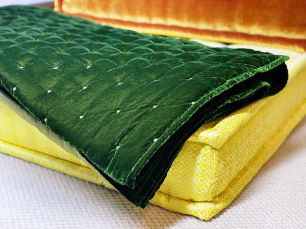 Close-up of layered green velvet throw and yellow cushion on the Mah Jong modular sofa, highlighting intricate fabric patterns.