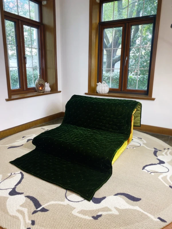 French daybed Mah Jong sofa with green velvet quilt and bright yellow accents, placed in a modern living room.