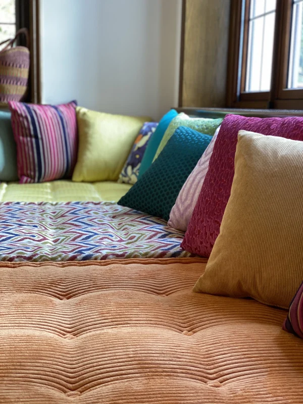 Side view of a Mah Jong daybed set against a bright window, showcasing plush pillows and multicolored cushions with intricate patterns.