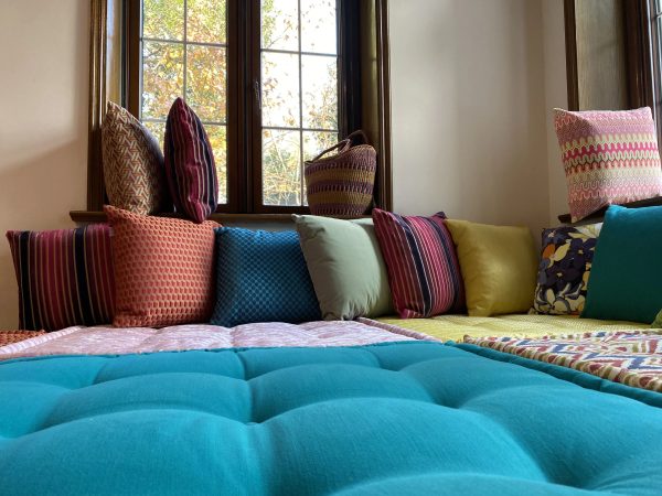 A vibrant Mah Jong daybed surrounded by light-filled windows, perfect for lounging with colorful pillows.