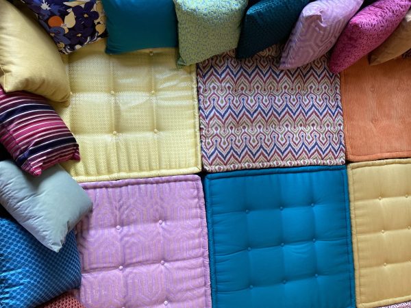 A colorful arrangement of tufted cushions in vibrant fabrics on a French-style Mah Jong daybed, featuring yellow, turquoise, and patterned designs.