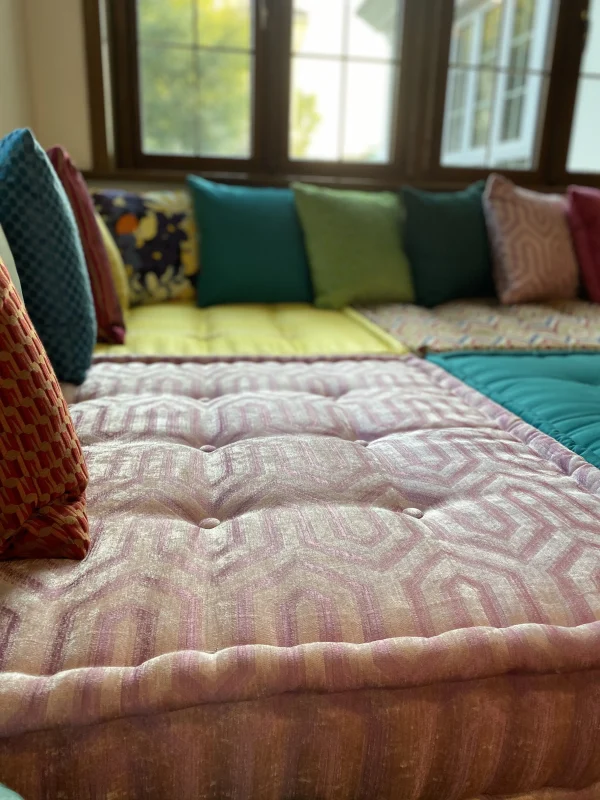 Colorful Mah Jong daybed featuring bold cushions and a zigzag pattern under natural lighting from a large window.