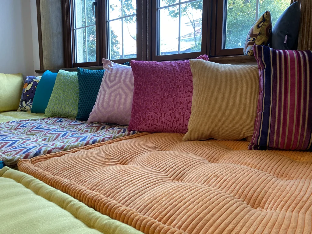 Close-up of a luxurious Mah Jong daybed with orange, yellow, and patterned cushions, offering modern French-inspired elegance.